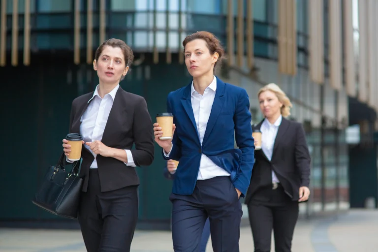 female-professionals-with-paper-coffee-cups-wearing-office-suits-walking-together-city-talking-discussing-project-chatting-front-view-businesswomen-outdoors-concept